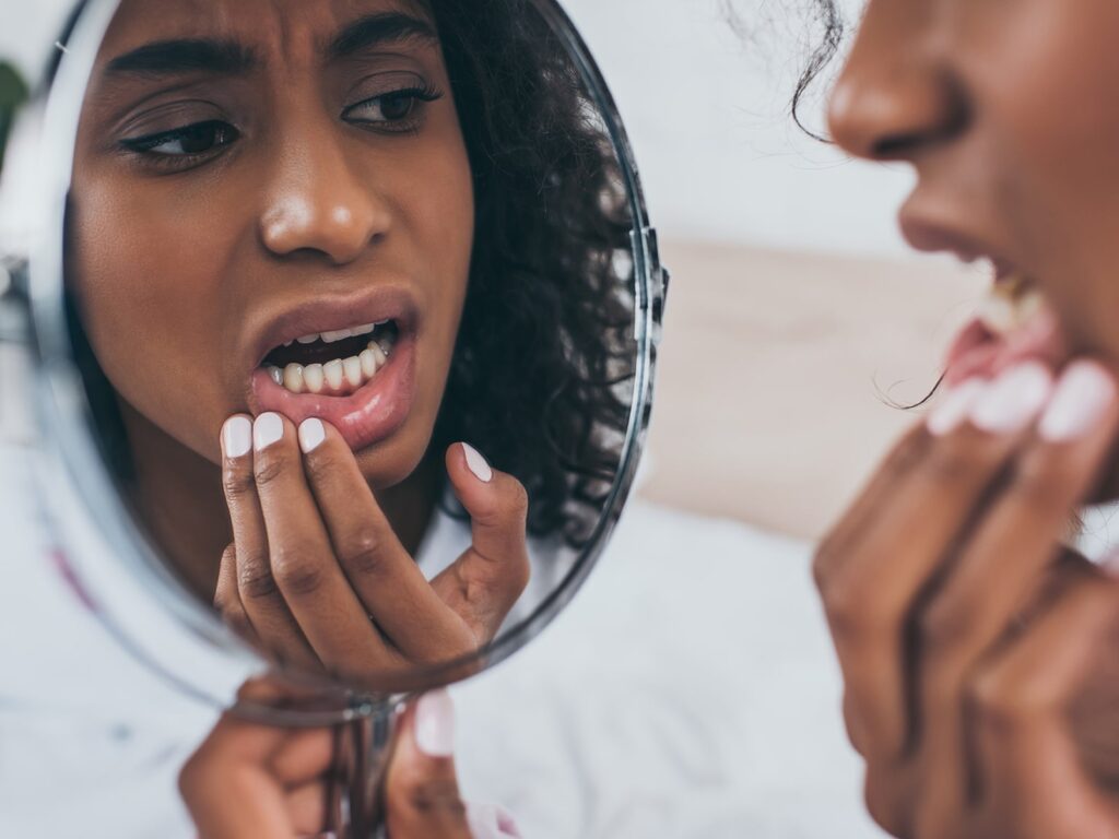 Woman inspecting gums and teeth in mirror closely.