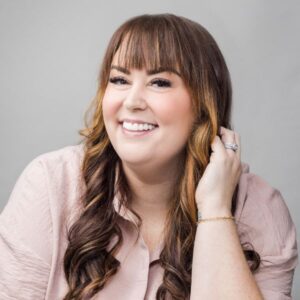 Smiling woman with long, wavy brown hair and bangs, showcasing a confident, radiant look, representing a life-changing smile transformation.