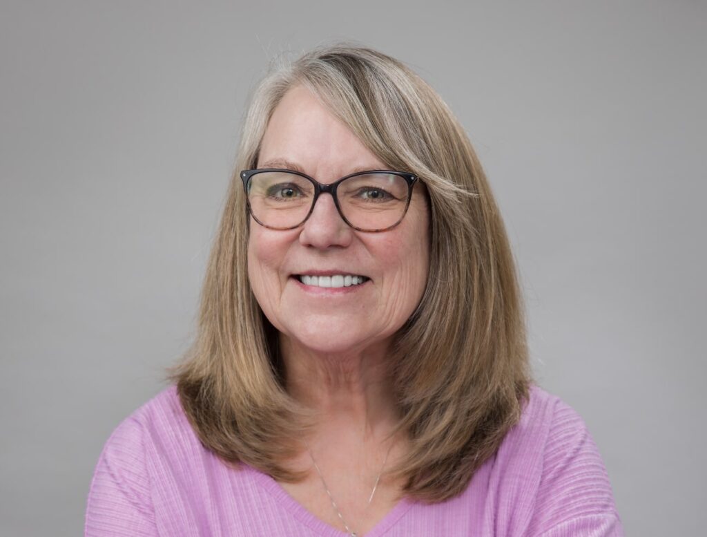 Middle-aged woman with light brown hair and glasses looking into the camera and smiling