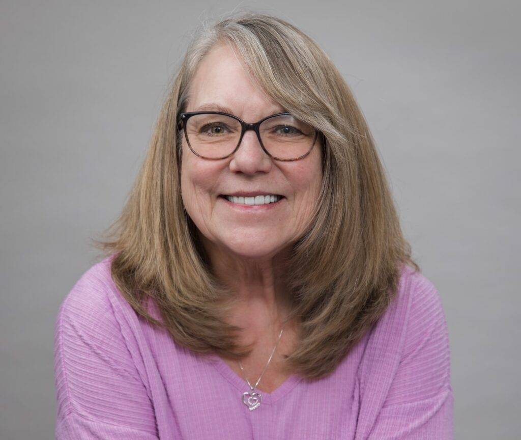 Middle-aged woman with light brown hair and glasses looking into the camera and smiling